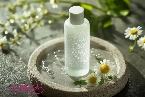 بطری شفاف تونر پوست با قطرات آب و گل بابونه در کنار آن