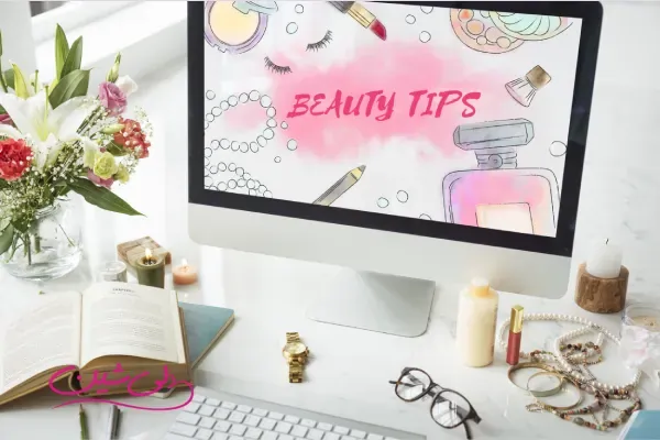 نمایی از میز کار زنانه با مانیتور شامل تصویر Beauty Tips، کتاب باز، لوازم آرایش و زیورآلات