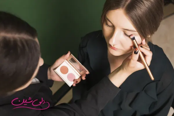 میکاپ آرتیست در حال آرایش چشم یک مدل با استفاده از پالت سایه و براش